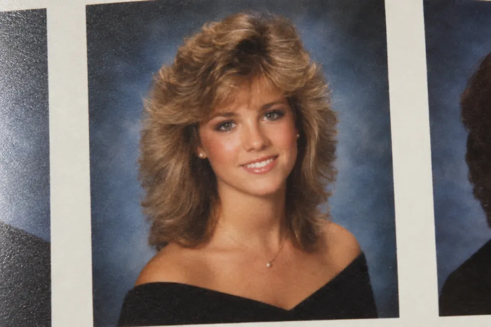 1980s yearbook portrait with feathered hair on a mottled blue studio backdrop